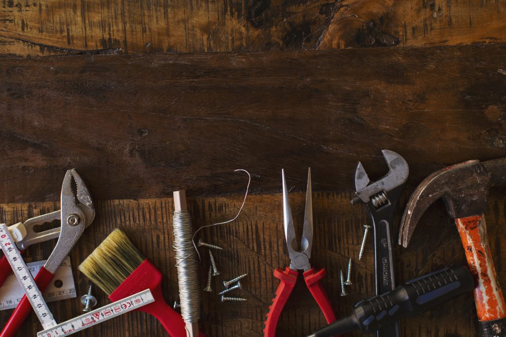 Flera olika sorters verktyg och tumstock ligger på en mörk träbänk.
